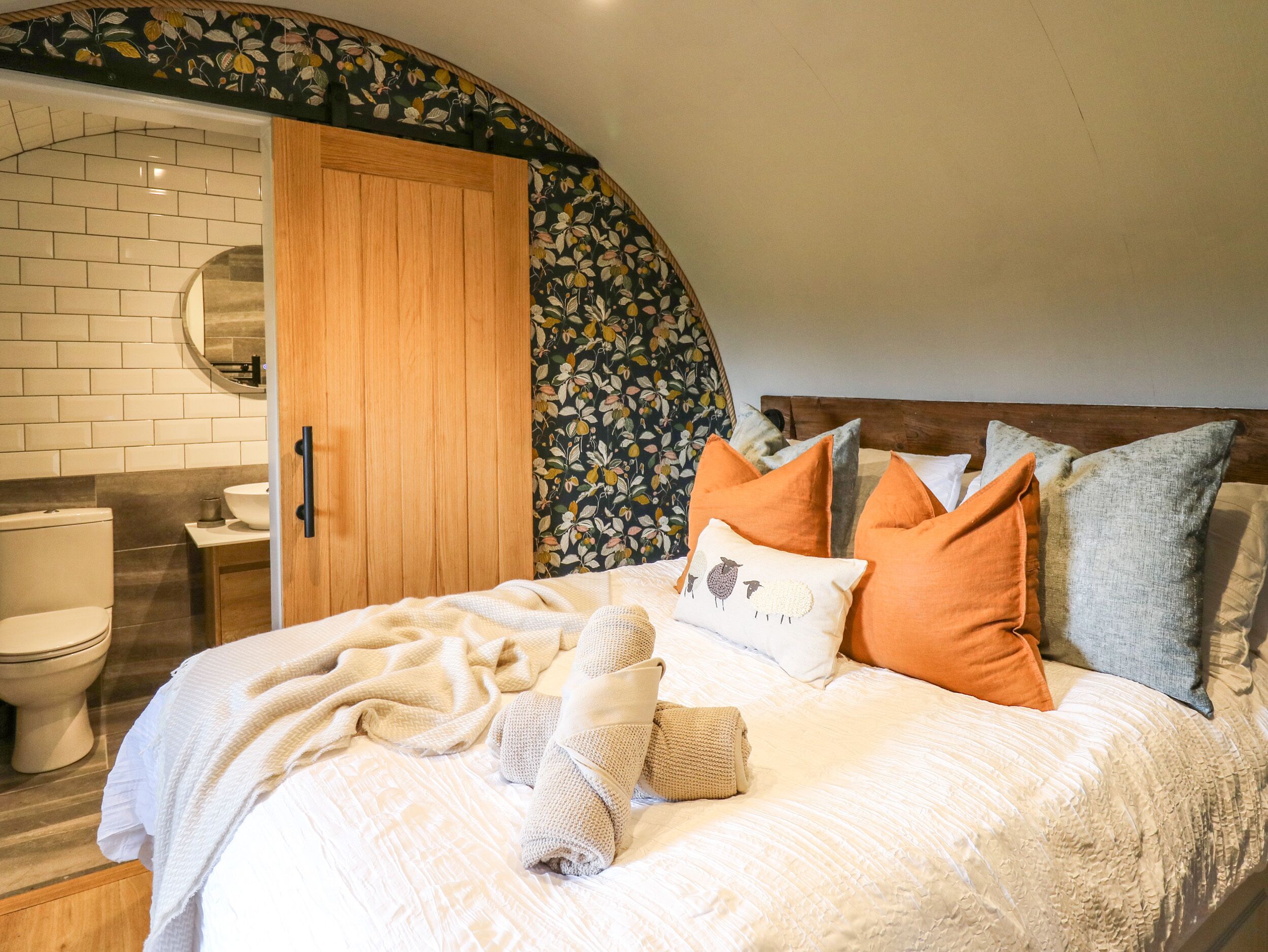 A bedroom with a bed, pillows, a blanket, a wooden wardrobe, and a bathroom with a toilet and sink.