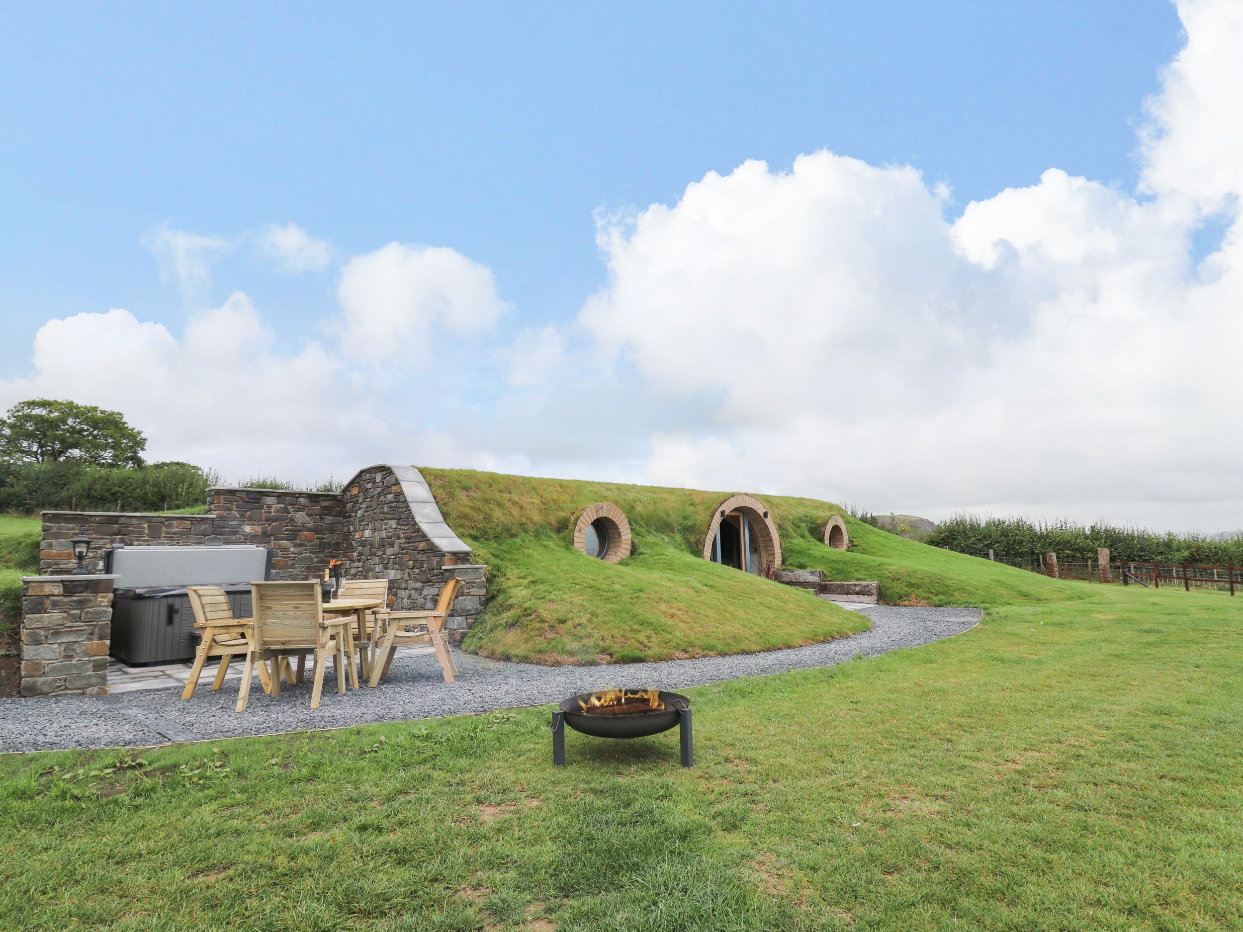 A stone building with a grassy hill, outdoor seating, and a fire pit.