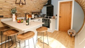 A kitchen with a central island, bar stools, a wooden ceiling, and a door leading to another room. - Tan Y Wawr - Derwen (Welshpool)