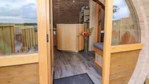 A wooden interior with a curved ceiling, a central wooden cabinet, and a small seating area with a cushion. - Tan Y Wawr - Derwen (Welshpool)