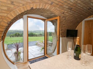 Una habitación con un amplio ventanal de arco que ofrece vistas a un paisaje verde. Se observa una zona de bar con una botella de champán y copas.
