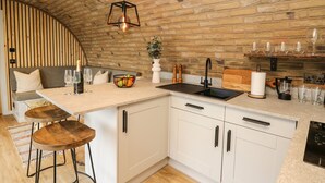 A kitchen with a wooden ceiling, white cabinets, a wooden bar stool, and a built-in sink. - Tan Y Wawr - Derwen (Welshpool)