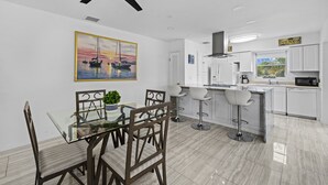A modern kitchen with white cabinets, a dining area with a glass table, and a ceiling fan. - Ship To Shore-Close to Beach (North Palm Beach)