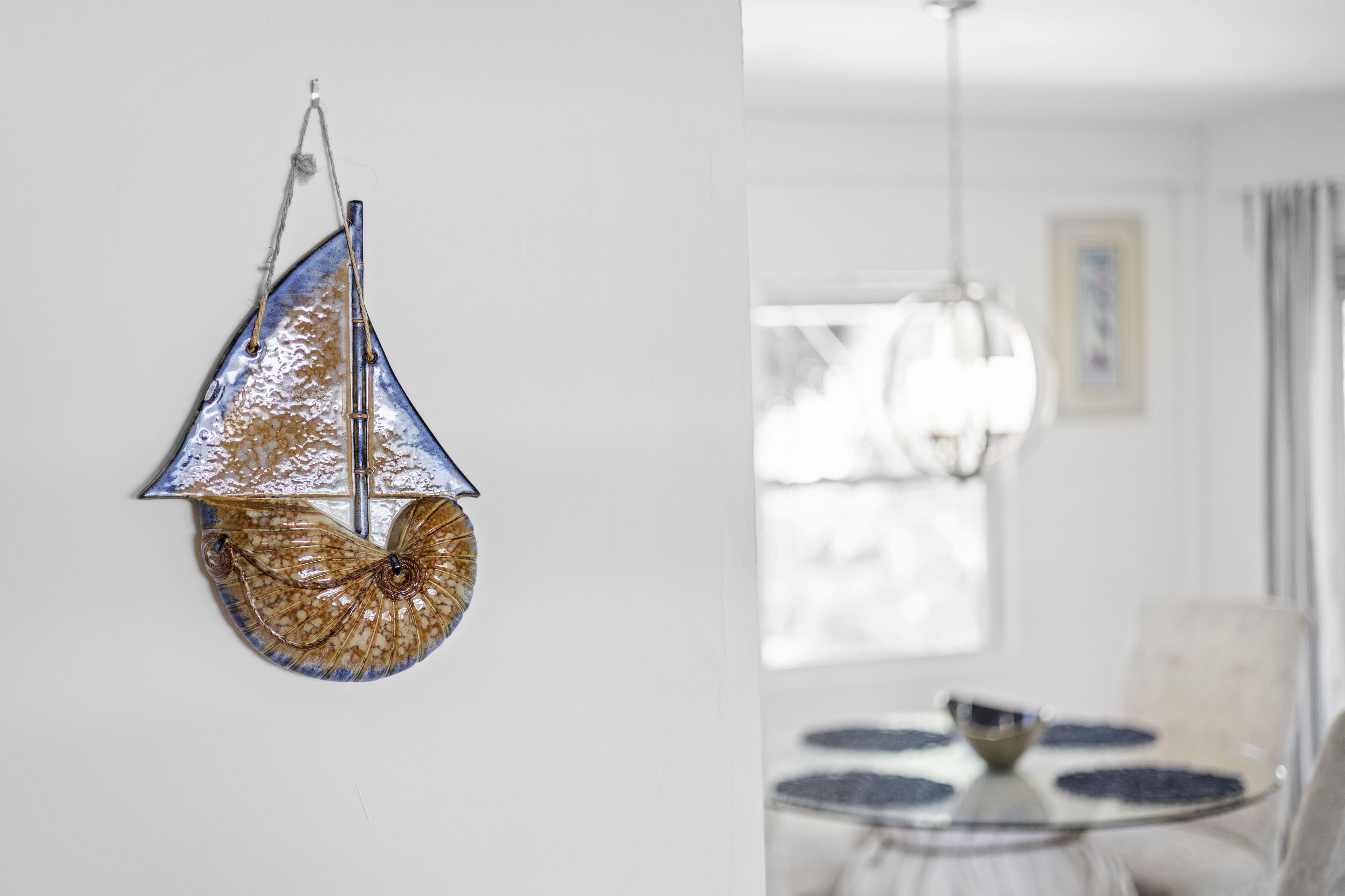 Een kamer met een ronde glazen tafel, een hanglamp en een ingelijst schilderij aan de muur.
