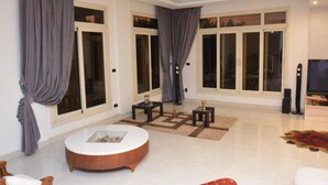 Uma sala de estar espaçosa com uma mesa de centro redonda, duas mesas laterais e uma TV de tela plana.
