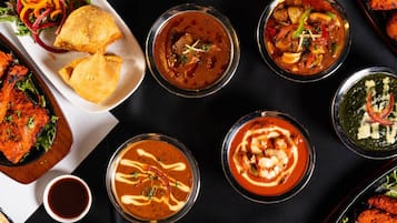 Diversos pratos, incluindo curry, arroz e carnes grelhadas, indicando uma experiência gastronômica variada.