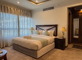 Un dormitorio ordenado con una cama grande, dos mesitas de noche con lámparas, un espejo y una ventana con cortinas estampadas.