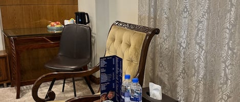 Une chambre d’hôtel dotée d’un coin repas comprenant une table en bois, un fauteuil en cuir noir, un fauteuil rembourré, un présentoir à menus, une bouteille d’eau et une boîte de mouchoirs.
