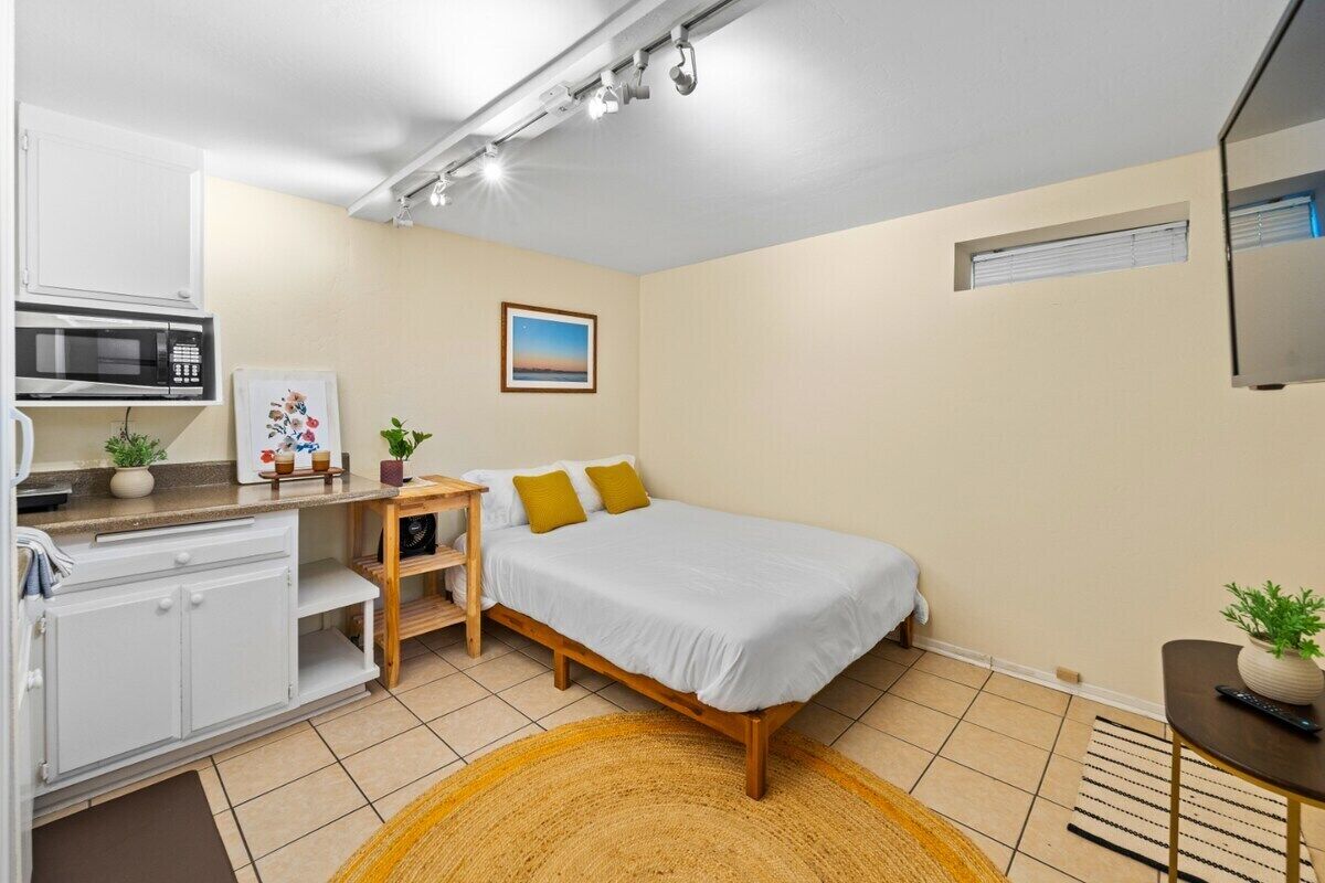 Une chambre à coucher de taille réduite, comprenant un lit, un bureau, un four à micro-ondes et une petite fenêtre.