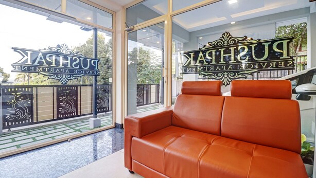A modern interior with a leather sofa, large glass windows, and a decorative sign. - Treebo Pushpak 500 mtrs from Chottanikkara temple (Kanayannur)