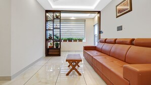 A modern living room with a brown leather sofa, a wooden coffee table, and a glass partition with potted plants. - Treebo Pushpak 500 mtrs from Chottanikkara temple (Kanayannur)