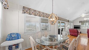 Un coin repas avec une table en verre et des chaises en osier, un ventilateur de plafond et une vue par la fenêtre.