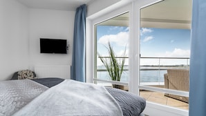 Ett sovrum med en säng, en tv, utsikt över havet och en balkong med en fåtölj i rotting.