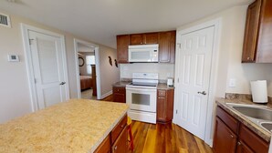 Una cocina compacta con armarios de madera, un microondas, un horno, un fregadero y una encimera de granito.