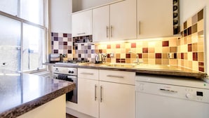 A modern kitchen with white cabinets, a granite countertop, a Bosch dishwasher, and a checkered backsplash. - JOIVY 1-Bed Flat In Edinburgh Old Town (Edinburgh)