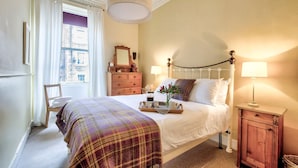 A neatly arranged bedroom with a bed, bedside lamps, a dresser, and a chair. - JOIVY 1-Bed Flat In Edinburgh Old Town (Edinburgh)