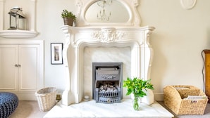 A white fireplace with a mantel, a chandelier, and a vase with green plants. - JOIVY 1-Bed Flat In Edinburgh Old Town (Edinburgh)