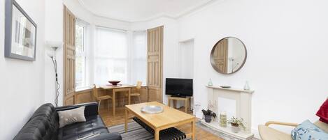 Una sala de estar moderna con un sofá de cuero negro, una mesa de centro de madera, un televisor y una chimenea.
