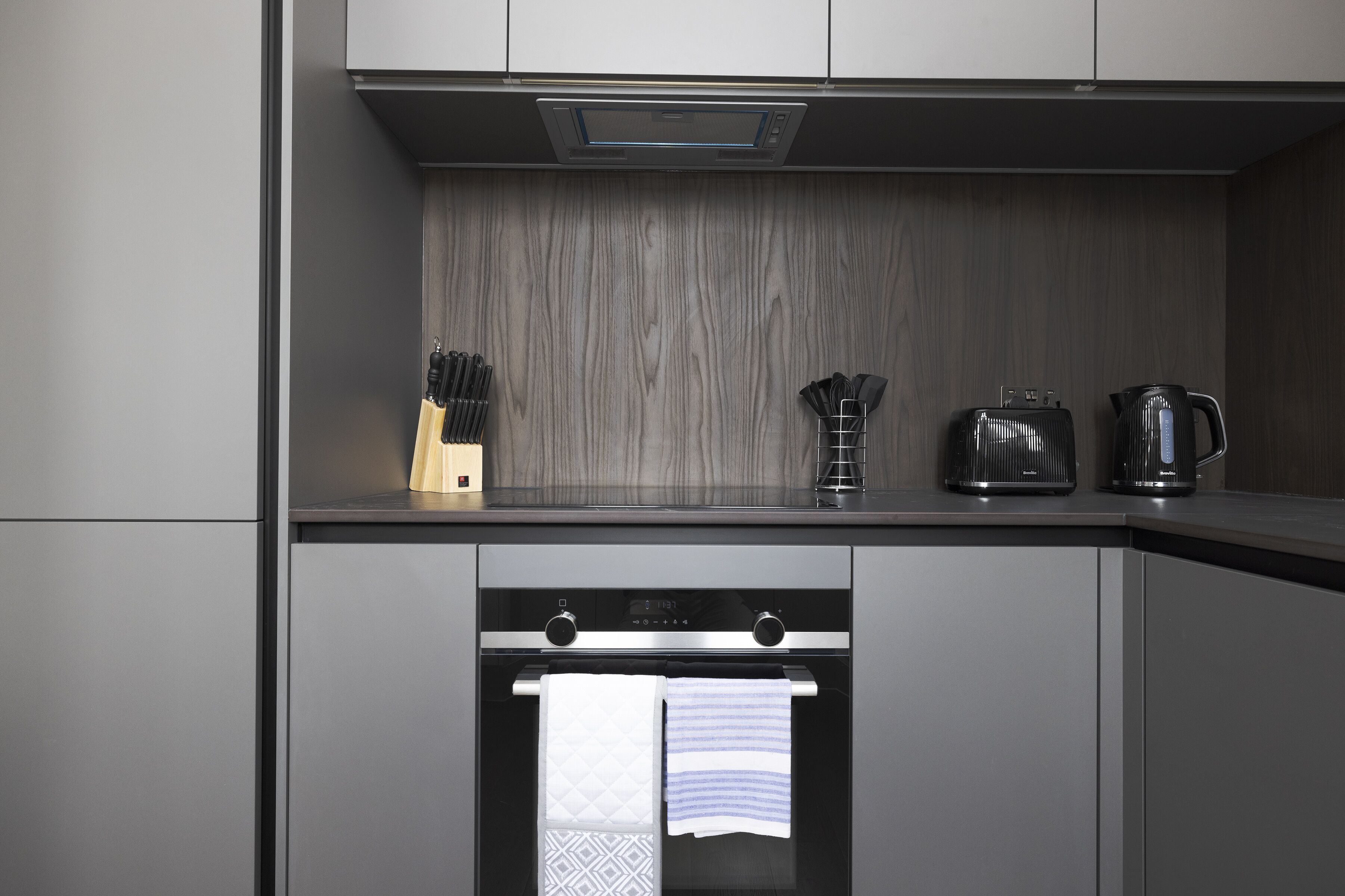 A modern kitchen with grey cabinetry, a built-in oven, and a coffee maker on the countertop.