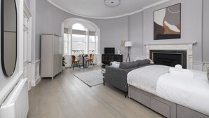 A modern bedroom with a fireplace, a large mirror, and a dining area with a view. - JOIVY Statement Studio On Historic George Street (Edinburgh)
