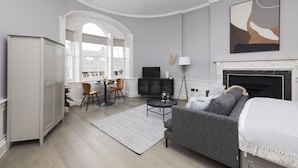 A modern living room with a fireplace, a sofa, a dining area, and a view of the city. - JOIVY Statement Studio On Historic George Street (Edinburgh)