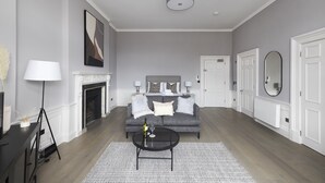 A modern living room with a grey sofa, a fireplace, a round coffee table, and a white door. - JOIVY Statement Studio On Historic George Street (Edinburgh)