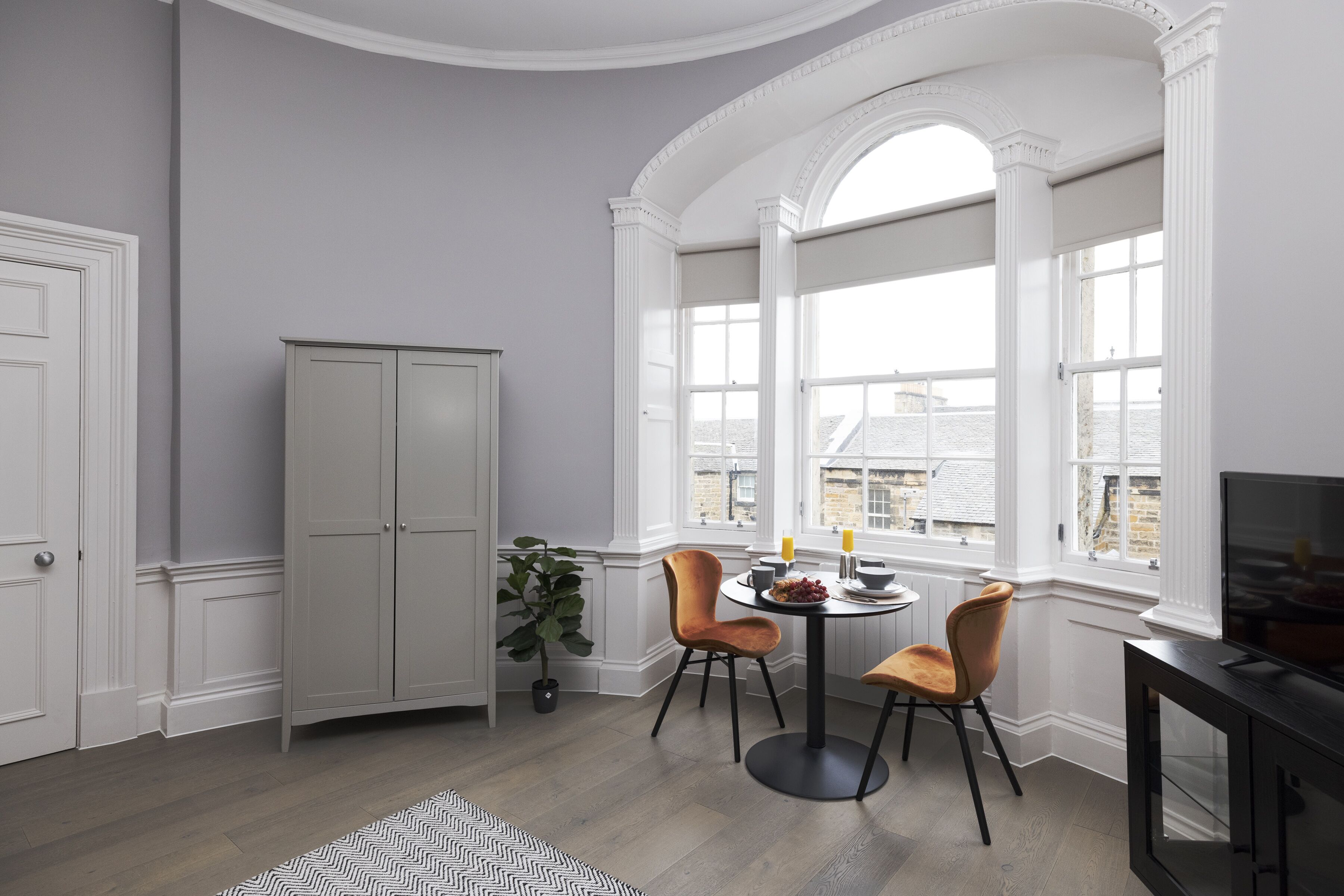 A room with a dining table, two chairs, a cabinet, and a television.