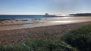 A beach with a clear sky and a large rock formation in the distance. - JOIVY Luxury House With Patio Next To North Berwick Beach (North Berwick)