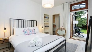 A bedroom with a bed, bedside table, lamp, and a view of the garden through a glass door. - JOIVY Luxury House With Patio Next To North Berwick Beach (North Berwick)