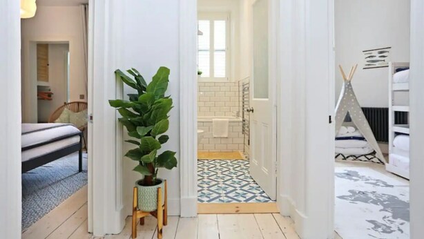 A hallway leading to a bathroom with a white bathtub, a potted plant, and a geometric-patterned floor. - JOIVY Luxury House With Patio Next To North Berwick Beach (North Berwick)