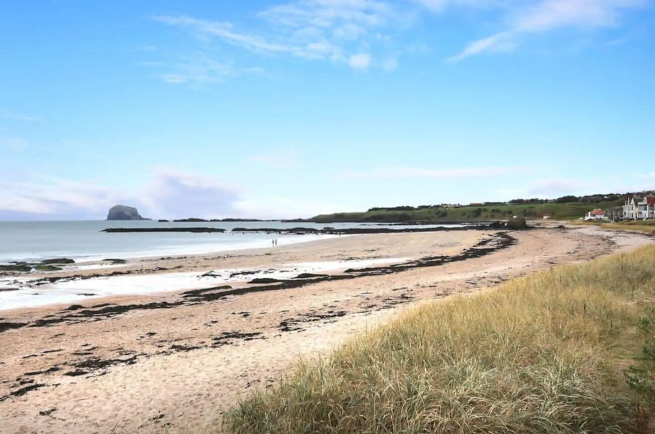 A beach with a sandy shore, a grassy area in the foreground, and a distant view of a building on a hill.