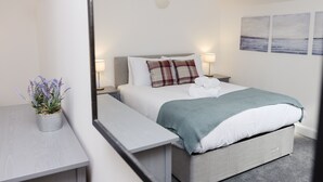 A modern bedroom with a bed, bedside tables, a nightstand, a lamp, and a wall-mounted shelf. - JOIVY Beautiful 2-Br Mews Home, Near Princes Street (Edinburgh)