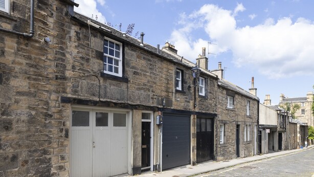 A stone building with a garage door, a small window, and a street. - JOIVY Beautiful 2-Br Mews Home, Near Princes Street (Edinburgh)