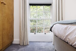 A bedroom with a window, a wooden wardrobe, and a bed with a grey blanket.