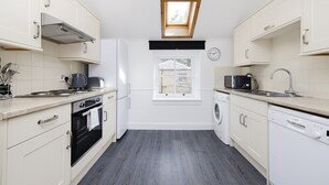 A compact kitchen with white cabinets, a built-in oven, a washing machine, and a skylight. - JOIVY Beautiful 2-Br Mews Home, Near Princes Street (Edinburgh)