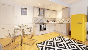 Una cocina moderna con armarios blancos, una mesa de comedor de vidrio y un refrigerador amarillo.