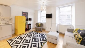 Una sala de estar moderna con un tapete estampado, un refrigerador amarillo, un sofá gris y una araña.