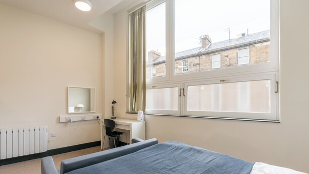 A bedroom with a bed, a desk, a chair, a window, and a radiator. - JOIVY Meadows Park En-Suite Rooms (Edinburgh)