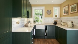 A modern kitchen with dark green cabinets, a white countertop, a sink, and a window with a view of greenery. - JOIVY The East Lodge At Balcarres (Leven)