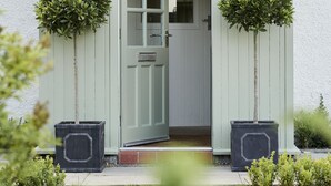 A light green shed with a door, two potted plants, and a small window. - JOIVY The East Lodge At Balcarres (Leven)