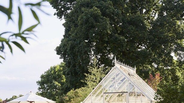 A greenhouse with a checkered floor, surrounded by lush greenery and a picnic table with benches. - JOIVY The East Lodge At Balcarres (Leven)