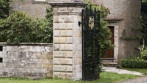 A stone building with a conical roof, a statue on a pedestal, and a black iron gate.