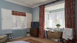 Une chambre à coucher avec un grand lit, une commode, une coiffeuse avec un miroir, une baignoire et une fenêtre avec des rideaux.