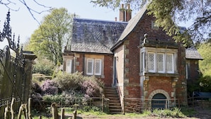 Une maison traditionnelle en pierre, dotée d’un toit à forte pente, d’un petit porche à l’avant et d’une entrée fermée par un portail.