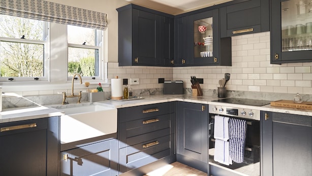 Une cuisine moderne avec des meubles de couleur sombre, un plan de travail blanc et un four encastré.