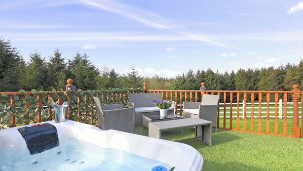 A hot tub with a control panel, surrounded by wicker furniture and a small table with a potted plant. - JOIVY Greenknowes Cottage W/ Hot Tub & Fireplace (Kelty)