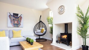 A living room with a sofa, a hanging chair, a wooden coffee table, a fireplace, and a painting on the wall. - JOIVY Greenknowes Cottage W/ Hot Tub & Fireplace (Kelty)