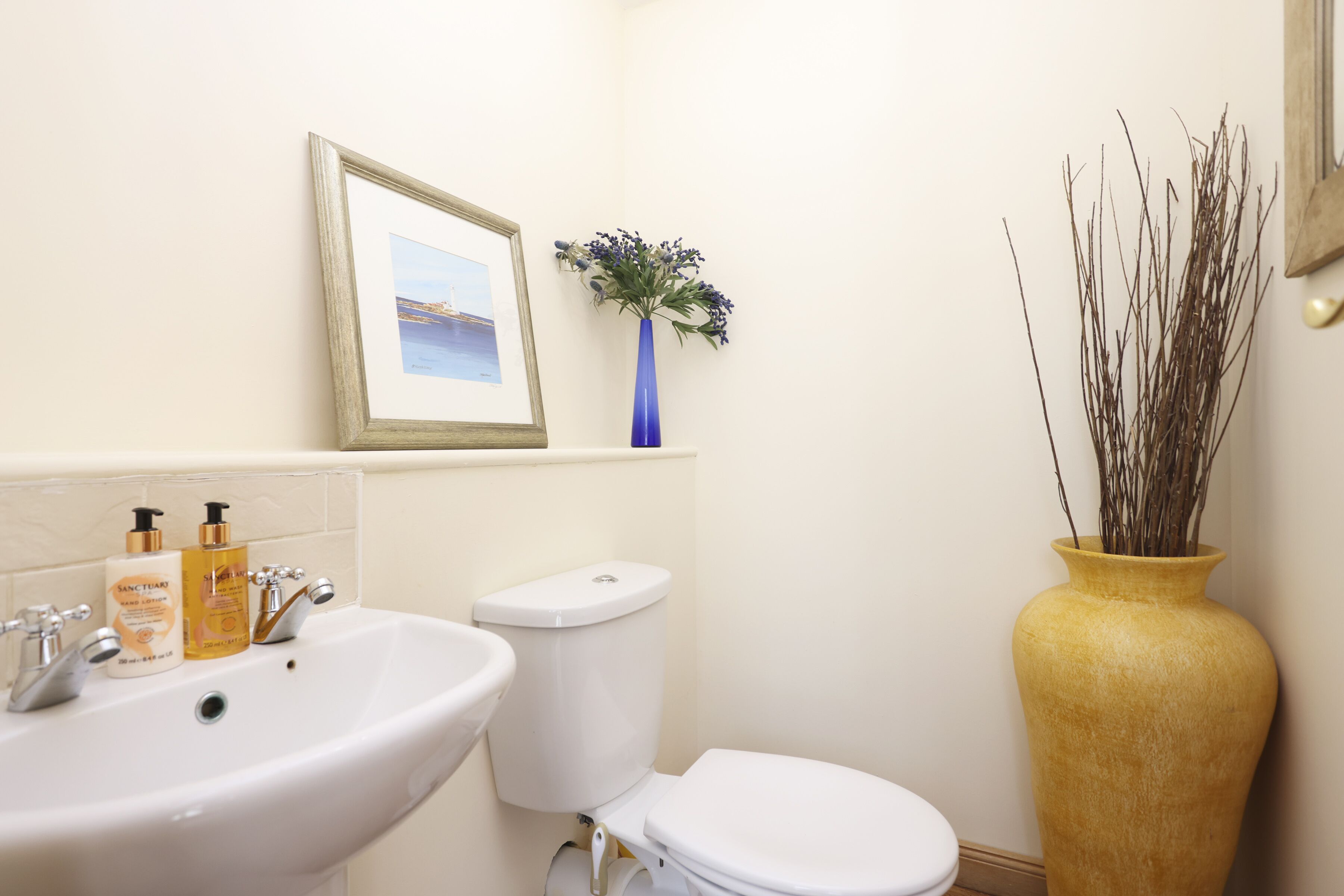 A bathroom with a white sink, toilet, and a vase with branches.