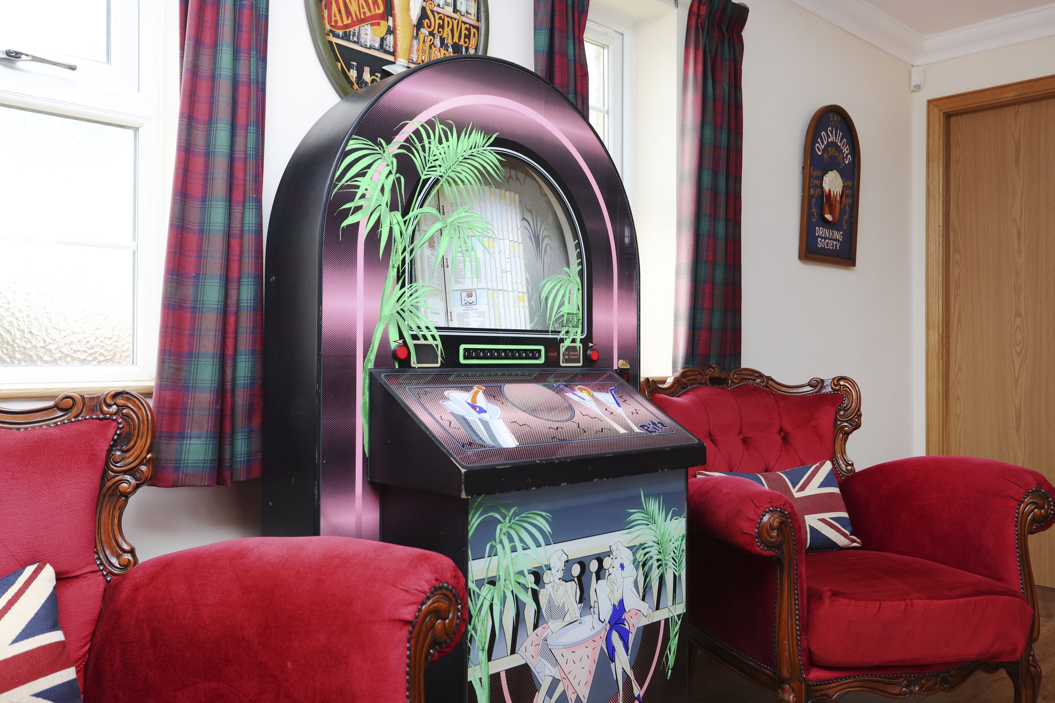 A room with a jukebox, red upholstered chairs, and a door.