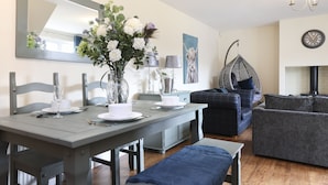 A dining area with a table set for four, a hanging chair, and a sofa. - JOIVY Greenknowes Lodge With Hot Tub And Wood Burning Stove (Kelty)